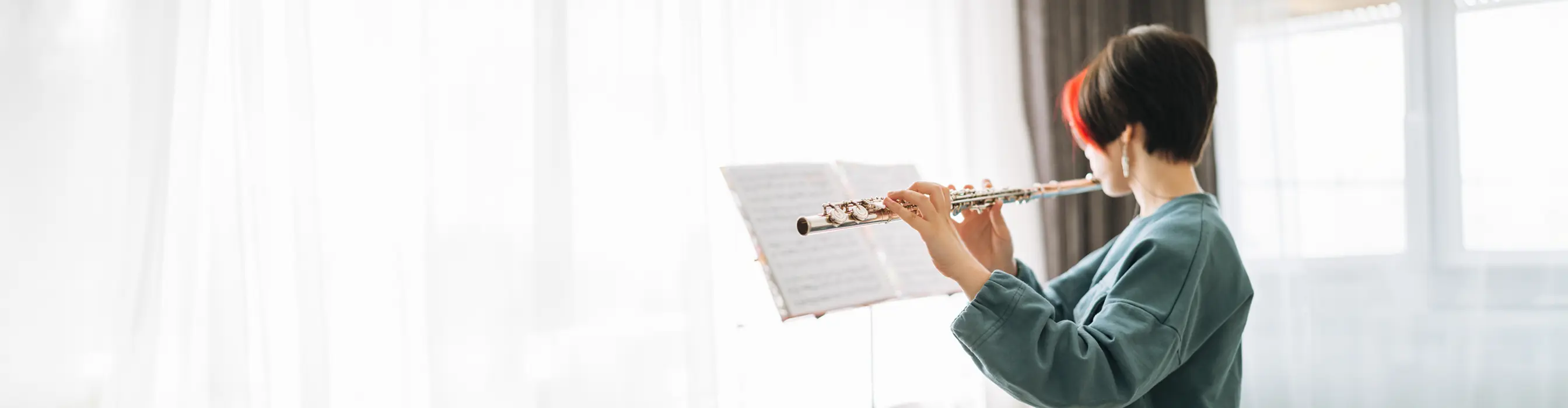 A girl with short red and brown hair playing the flute and reading music on a music stand
