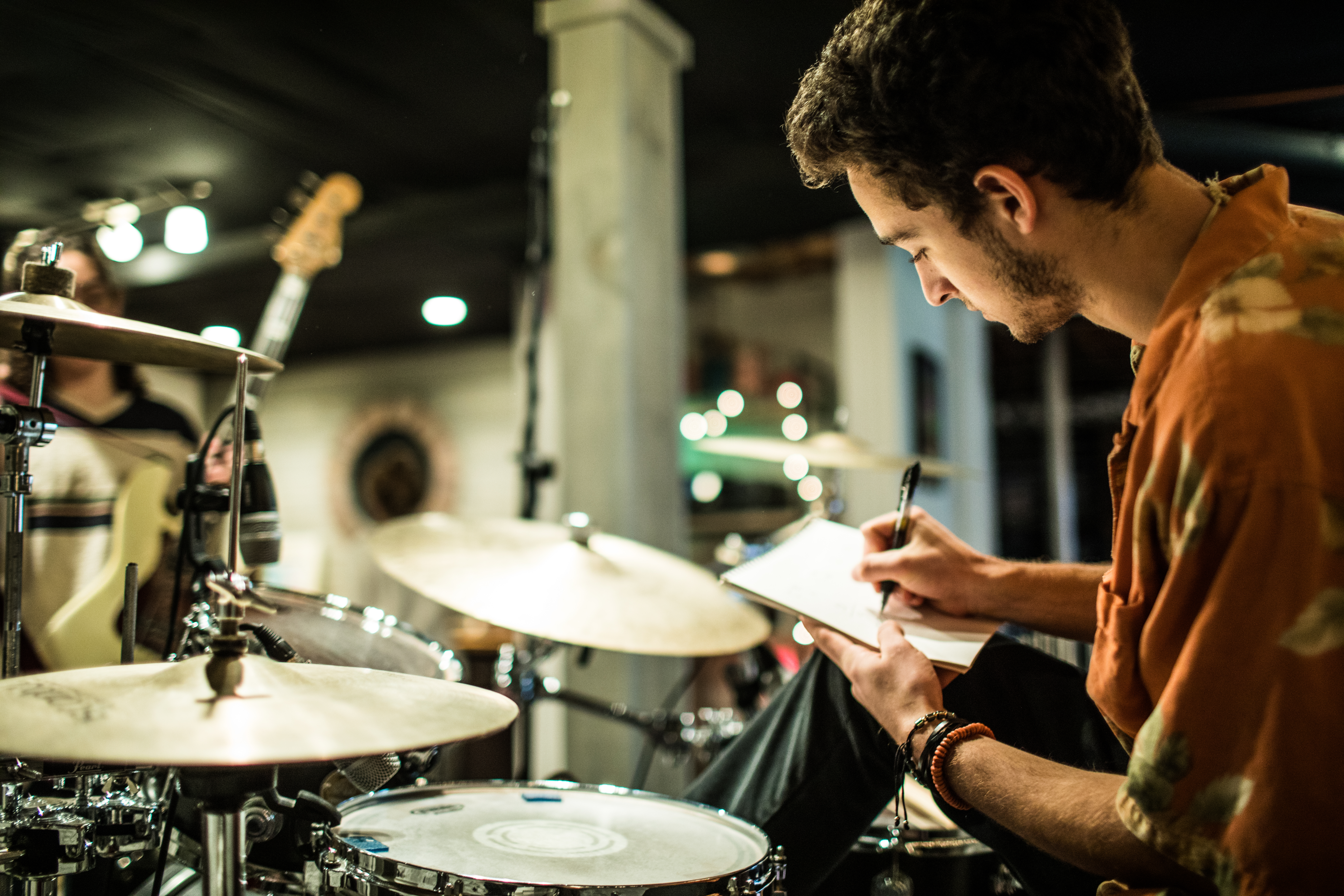 A man sat a drum kit, taking notes on a notepad