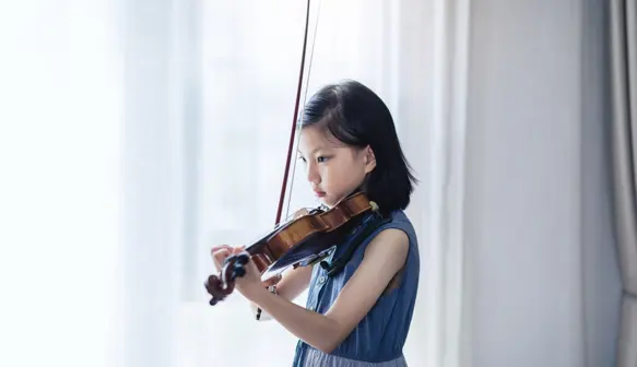 A young girl playing violin in front of a window
