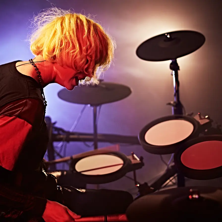 Man with long blonde hair playing an electric drum kit