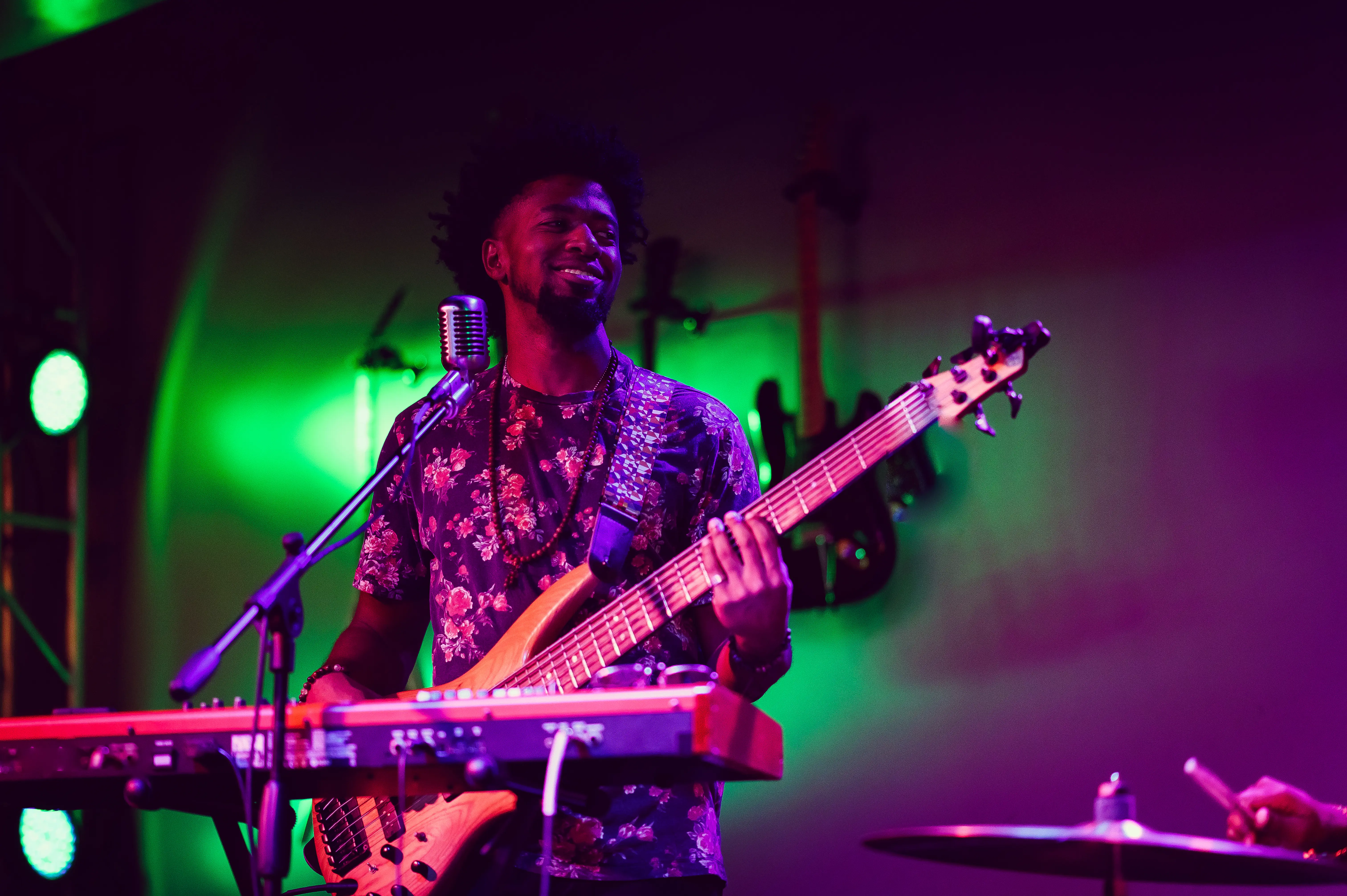 A man playing guitar on stage with a microphone and keyboard in front of him, moody colourful lighting